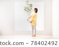 一個微笑的年輕女子拿著室內植物，盯著綠葉 78402492