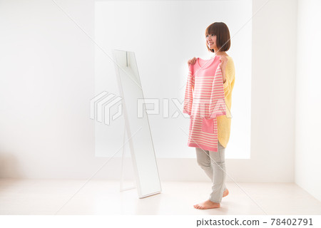 一位年輕女子試圖在鏡子前穿上粉紅色條紋衣服 一位年輕女子試圖在鏡子前穿上粉紅色條紋衣服 78402791