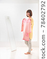 一位年輕女子試圖在鏡子前穿上粉紅色條紋衣服 78402792