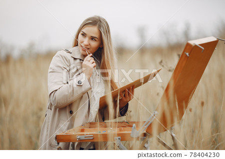 Woman in a brown coat painting in a field 78404230