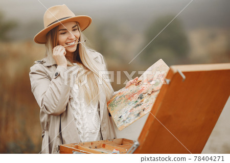 Woman in a brown coat painting in a field Woman in a brown coat painting in a field 78404271
