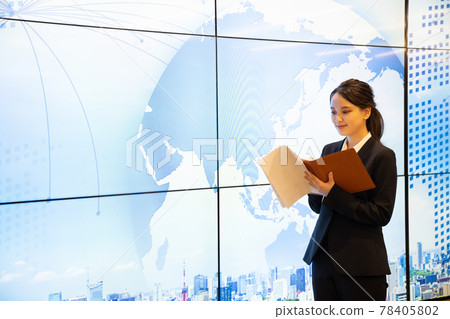 A young woman taking notes in her personal organizer in front of a large display 78405802