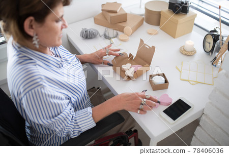 Disabled mature woman in wheelchair packing handmade products indoors at home, small business concept. 78406036