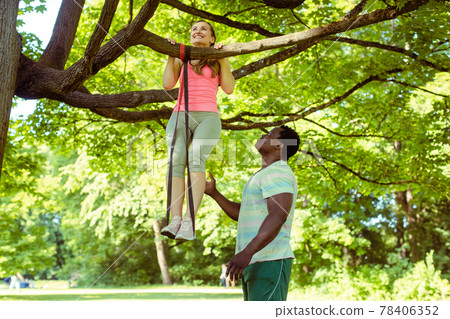 Woman doing pull-up assisted by her fitness coach on tree 78406352
