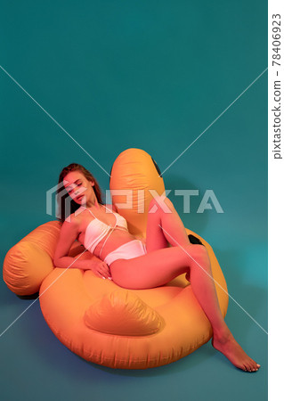Young woman in bikini sitting on yellow inflatable toy Young woman in bikini sitting on yellow inflatable toy 78406923
