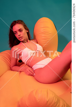 Dreamy girl lying on yellow inflatable pillow on blue background Dreamy girl lying on yellow inflatable pillow on blue background 78406924