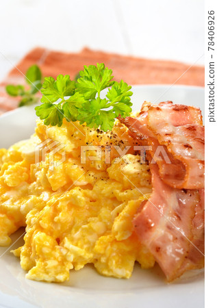 Scrambled eggs with fried bacon on a white plate 78406926