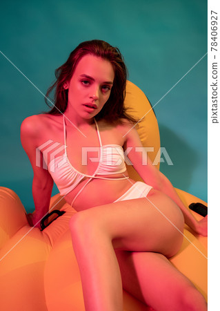 Girl in swimsuit sitting on yellow inflatable pool float on blue background Girl in swimsuit sitting on yellow inflatable pool float on blue background 78406927