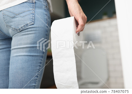 Woman holds roll of toilet paper in her hand while going to toilet 78407075