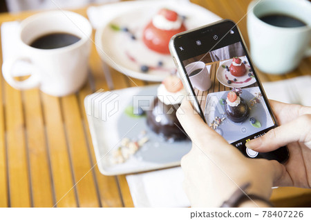A young woman taking a picture of a cake with her smartphone 78407226