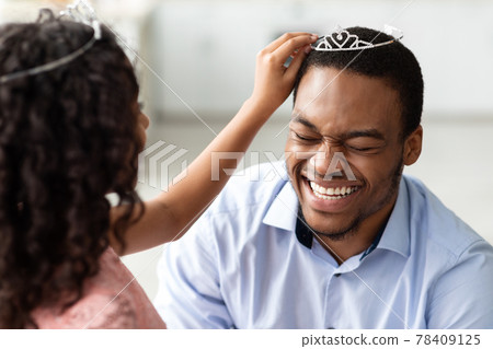 Curly little girl putting crown on her laughing father 78409125