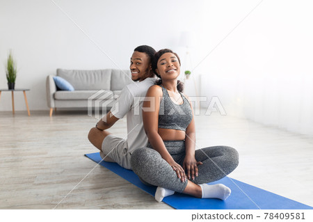 Smiling African American couple relaxing after yoga practice, sitting on fitness mat back to back, smiling at camera 78409581