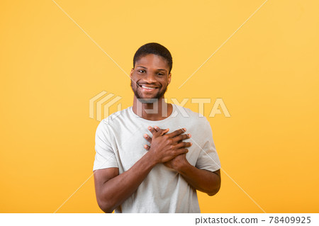 Pleased guy keeping palms on heart, feeling hope and love over yellow background, studio shot 78409925
