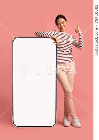 Cheerful Korean Lady Leaning At Big Blank Smartphone And Showing Thumb Up 78410082