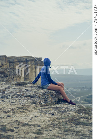 Woman sits on a rock, looking at the landscape and enjoying the view and fresh air. Woman sits on a rock, looking at the landscape and enjoying the view and fresh air. 78411737