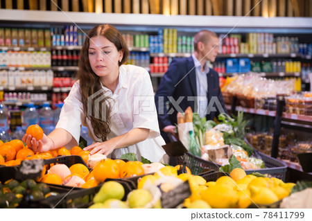 Focused young girl selects ripe tangerines in a supermarket 78411799