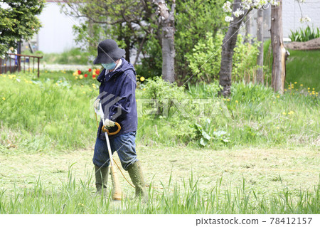 一位中年婦女用家用電動割草機割花園 78412157