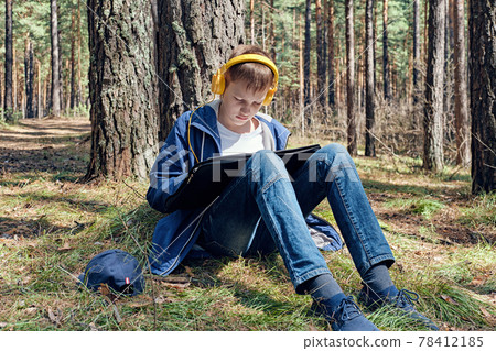 Young artist sits in pine forest and plein air painting and listens to music. Sunny day, creative leisure 78412185