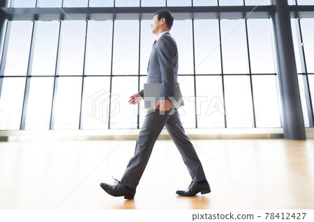 Middle-aged businessman walking with a laptop 78412427