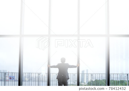 The back view of a businessman looking out with his hand on the window 78412432
