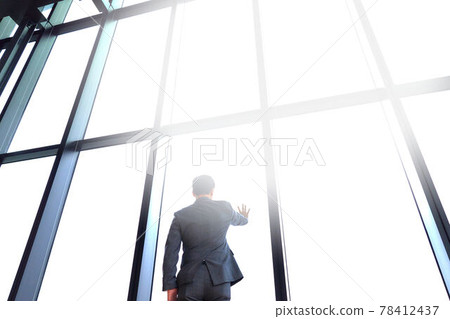 The back view of a businessman looking out with his hand on the window 78412437