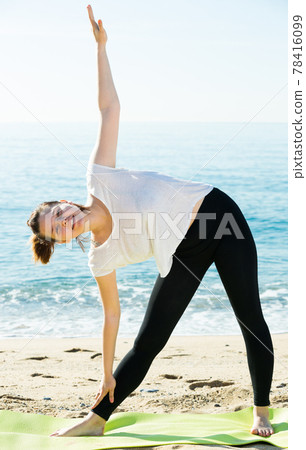 Athletic woman in white T-shirt is practicing set of stretching exercises 78416099