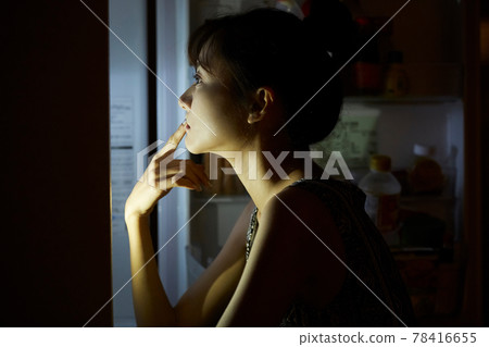 Young woman eating late at night 78416655