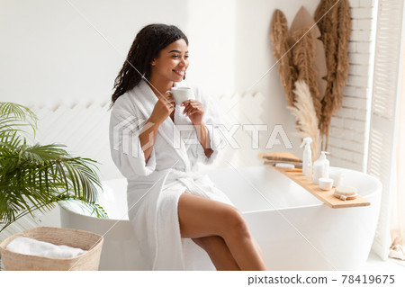 Happy African Lady Drinking Coffee Sitting On Bathtub In Bathroom Happy African Lady Drinking Coffee Sitting On Bathtub In Bathroom 78419675