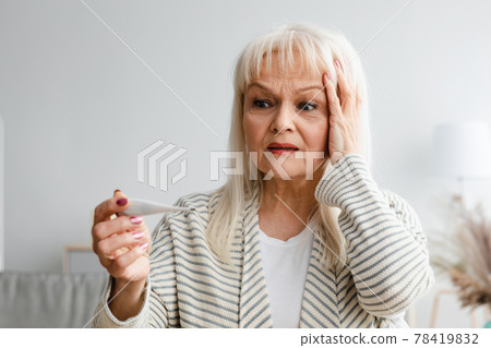 Scared mature woman checking body temperature looking at thermometer 78419832