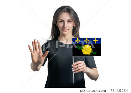 Happy young white woman holding flag of Guadeloupe and with a serious face shows a hand stop sign isolated on a white background 78419984