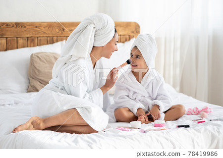 Young mother touching her cute daughter nose with brush Young mother touching her cute daughter nose with brush 78419986