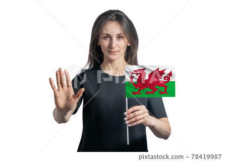Happy young white woman holding flag of Wales and with a serious face shows a hand stop sign isolated on a white background Happy young white woman holding flag of Wales and with a serious face shows a hand stop sign isolated on a white background 78419987