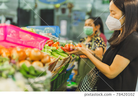 Woman in protective mask chooses tomatoe in vegetable store. 78420102