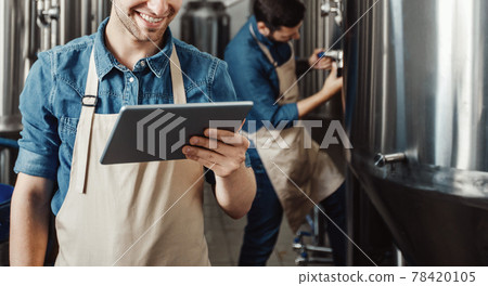 Beer production process at brewery. Man operating brewing equipment at beer making factory and using digital tablet Beer production process at brewery. Man operating brewing equipment at beer making factory and using digital tablet 78420105