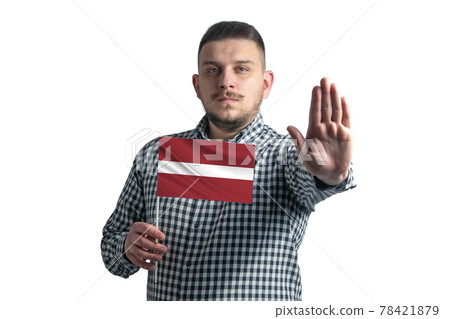 White guy holding a flag of Latvia and with a serious face shows a hand stop sign isolated on a white background 78421879