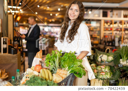 Positive young woman with shopping cart at supermarket 78422439