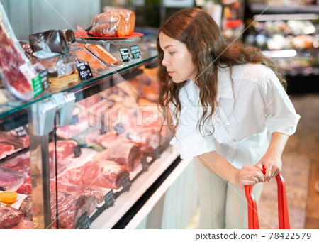 Young girl examines the production in the department of the butcher shop in the supermarket 78422579