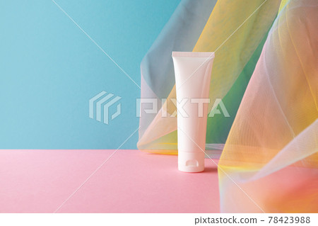 White plastic tube for beauty product on blue pink background with colorful rainbow organza fishnets fabric drapery 78423988