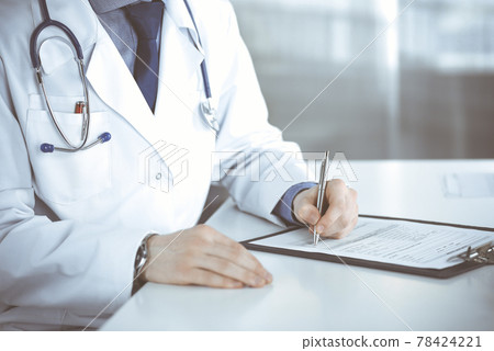 Unknown male doctor sitting and working with clipboard of medication history record in clinic at his working place, close-up. Young physician at work. Perfect medical service, medicine concept 78424221