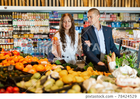 Happy young couple with a grocery cart in the supermarket shooses tangerines 78424529