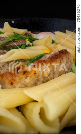 Tasty cutlet with eggs lie in black frying pan among pasta 78426276