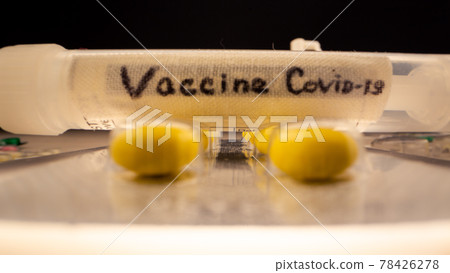 Small syringe with covid-19 vaccine over yellow pills 78426278