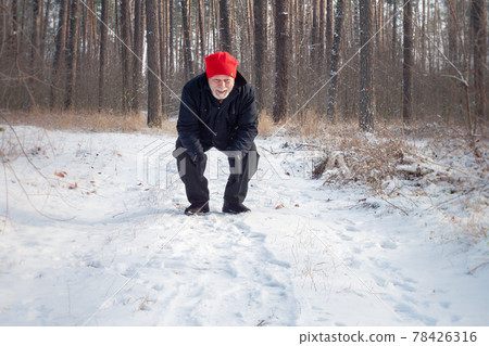 Old man in red hat stands on snowy road calling pet 78426316