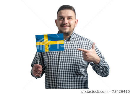 White guy holding a flag of Sweden and points the finger of the other hand at the flag isolated on a white background White guy holding a flag of Sweden and points the finger of the other hand at the flag isolated on a white background 78426410