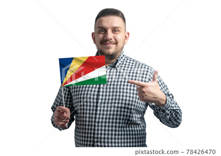 White guy holding a flag of Seychelles and points the finger of the other hand at the flag isolated on a white background 78426470