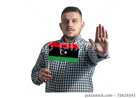 White guy holding a flag of Libya and with a serious face shows a hand stop sign isolated on a white background White guy holding a flag of Libya and with a serious face shows a hand stop sign isolated on a white background 78426845