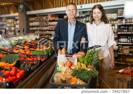 Portrait of a confident young couple with a grocery cart in the supermarket 78427667