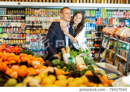 Glad couple is standing with cart with products in supermarket 78427684
