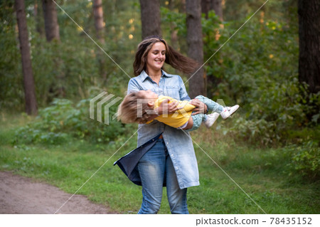 young mother is spinning with a baby in her arms. happy mom dancing with toddler on the background of nature and forest. mom and daughter laugh 78435152