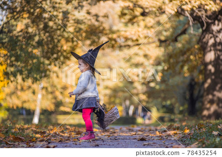 adorable little toddler girl in autumn park. girl in witch costume and black hat cosplay halloween costume. halloween celebration 78435254